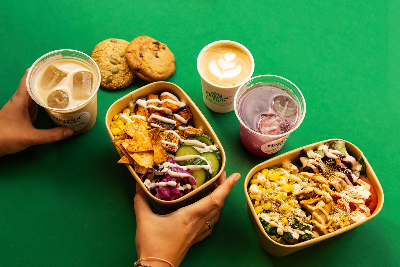 Een bowl, een salade, koffie, ijskoffie, huisgemaakte limonade en koekjes van Harvest Hub op een groene tafel